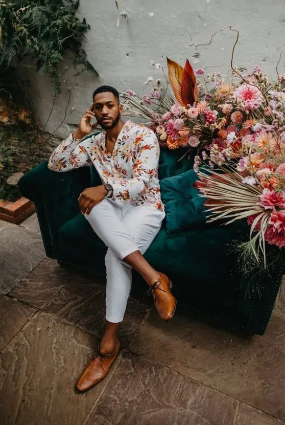 A bold summer wedding guest outfit with a bright printed shirt white trousers amber shoes is super cool