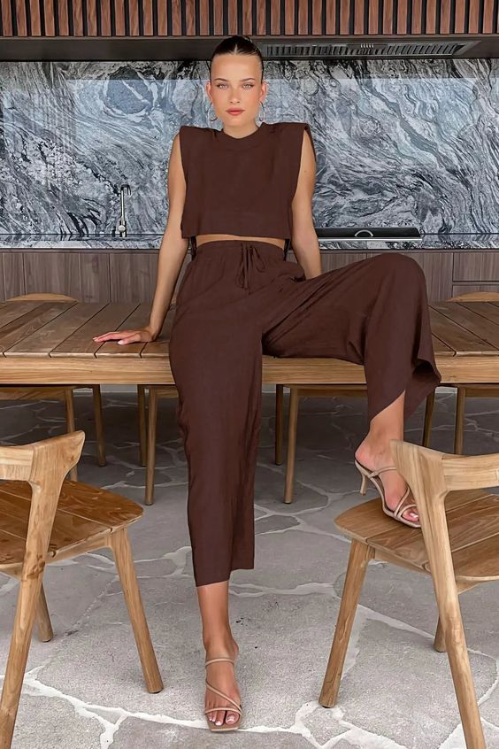 A brown linen combo of a sleeveless crop top and high waisted pants plus nude strappy shoes
