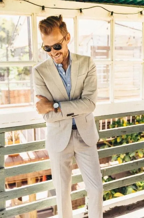 A relaxed and chic summer wedding guest outfit with a creamy pantsuit a blue linen shirt and sunglasses