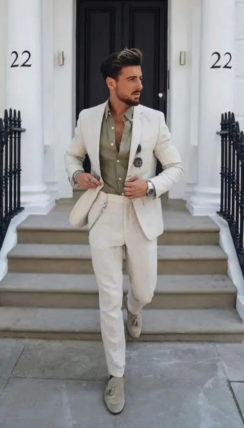 An effortlessly chic summer wedding guest look with an olive green shirt a creamy linen suit grey loafers and a chain