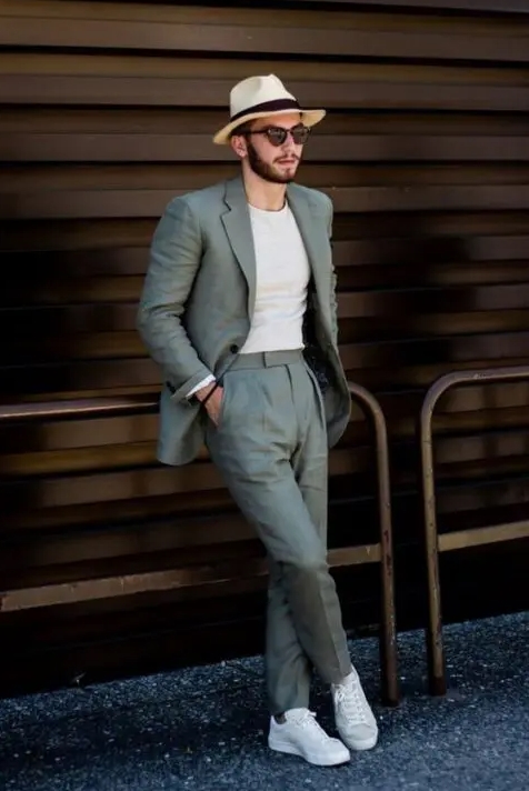 An informal summer wedding guest outfit with a grey pantsuit a white fitting t shirt white sneakers and a hat