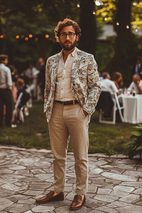 Tan linen pants a white linen button down a floral print blazer and brown shoes compose a fun look for a summer wedding