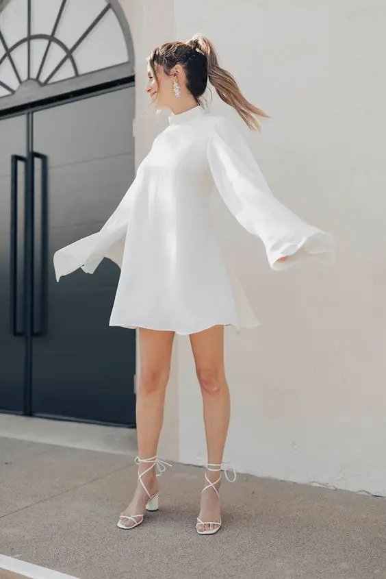 a classy bridal shower look with a white A line mini dress with a high neck flare sleeves and lace up shoes